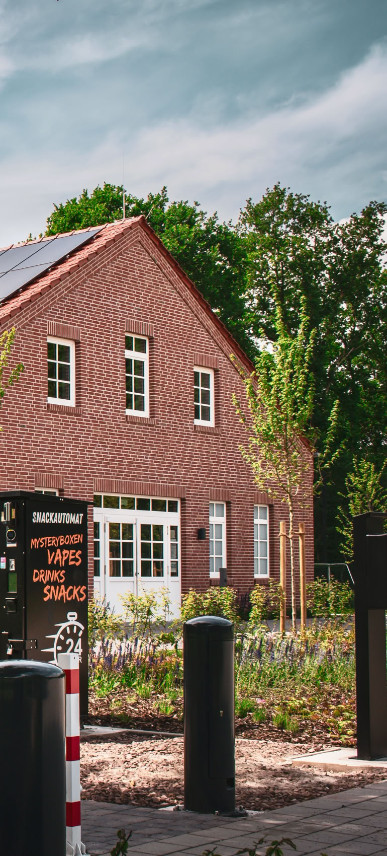 Backsteingebäude mit großen Fenstern, umgeben von Bäumen und einem gepflasterten Weg im Vordergrund.