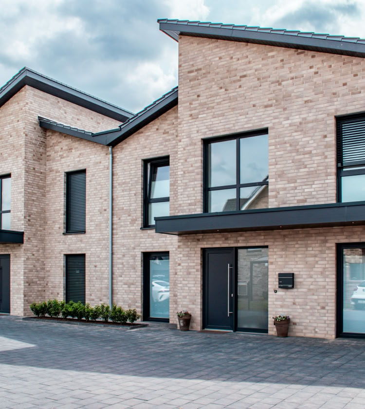 Modernes zweistöckiges Haus mit Ziegelfassade, großen Fenstern und einem gepflasterten Vorhof.